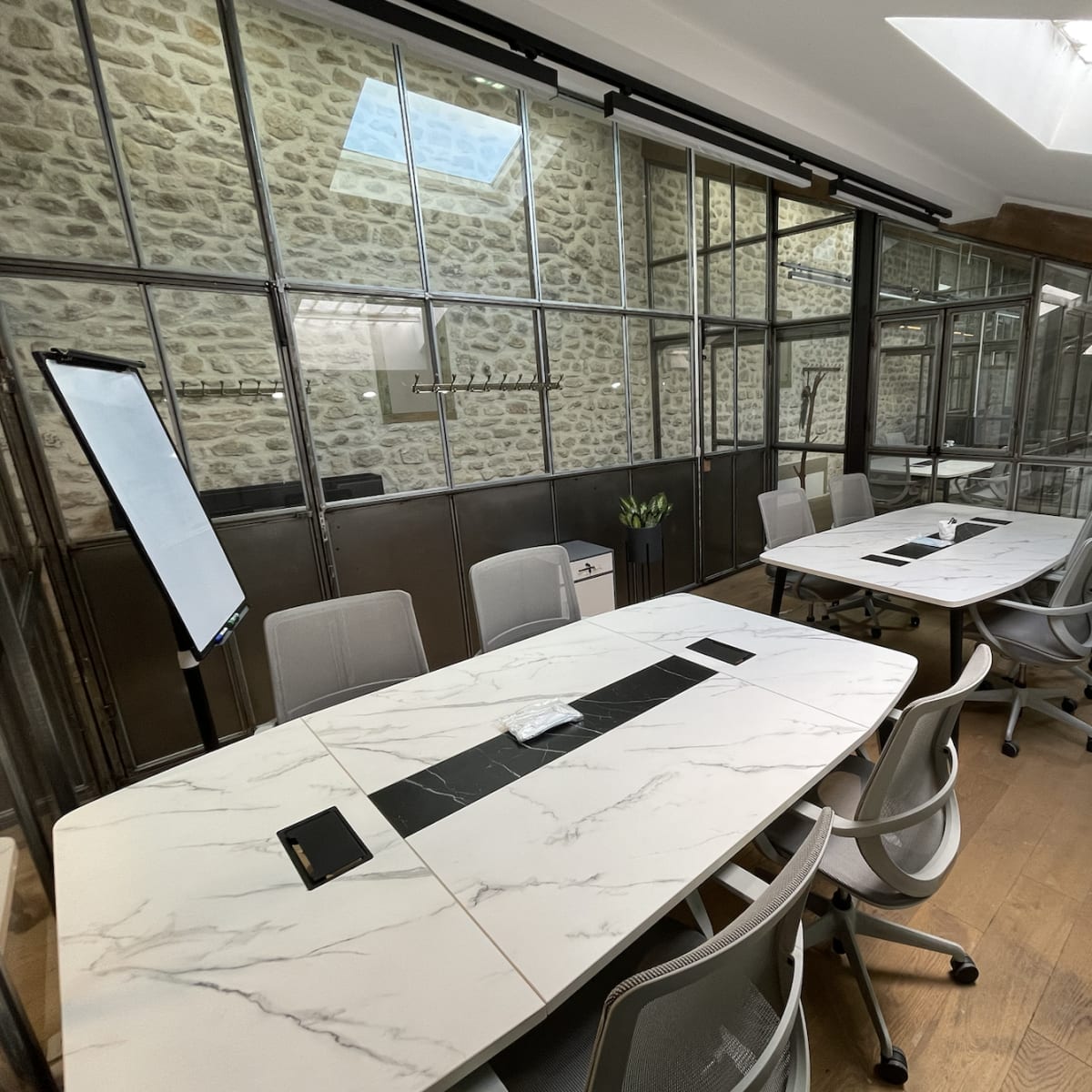 A modern conference room features glass walls, a large marble table, and ergonomic chairs, with natural light streaming through a skylight.