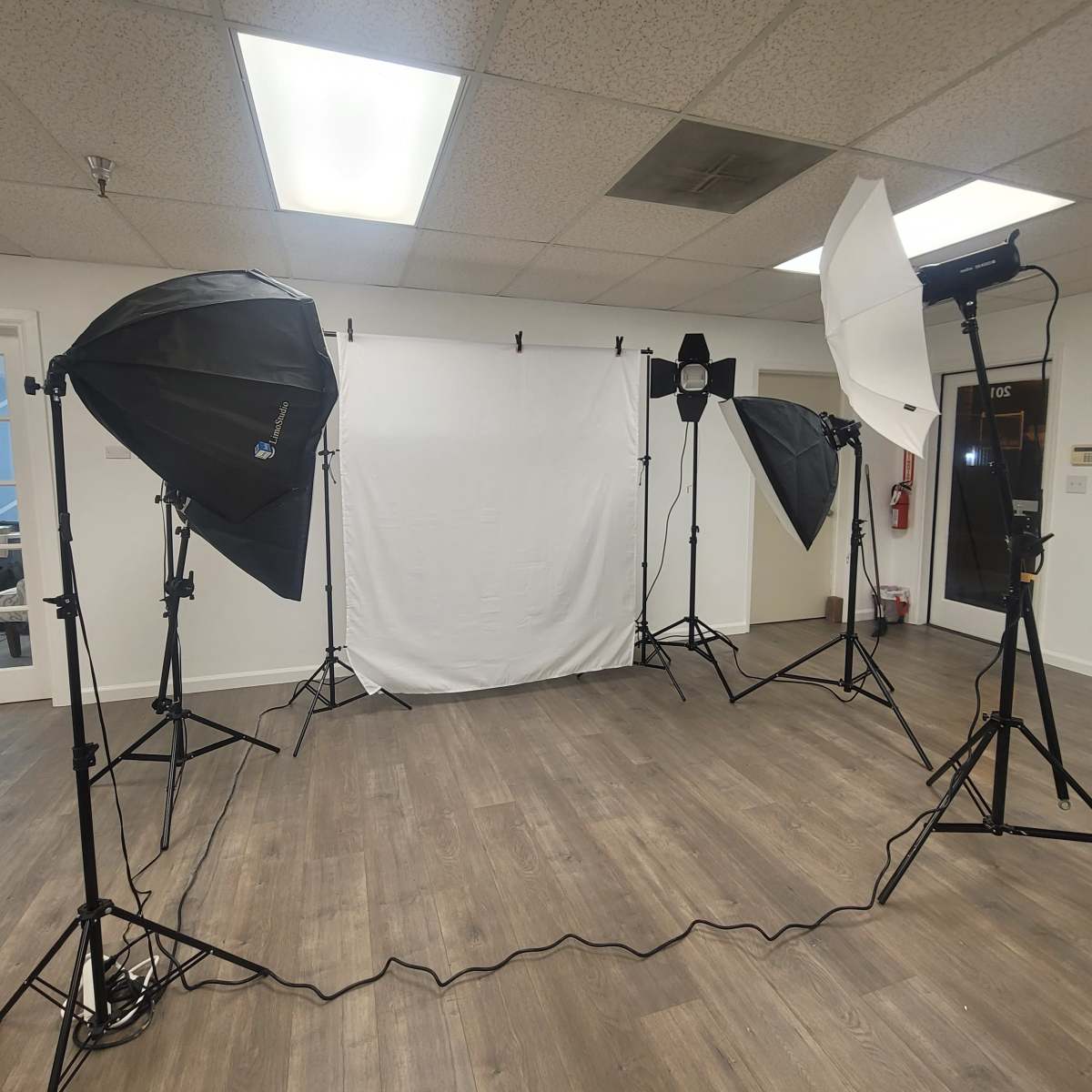 A photography studio setup with several softboxes, a light stand, and a backdrop on a wooden floor.