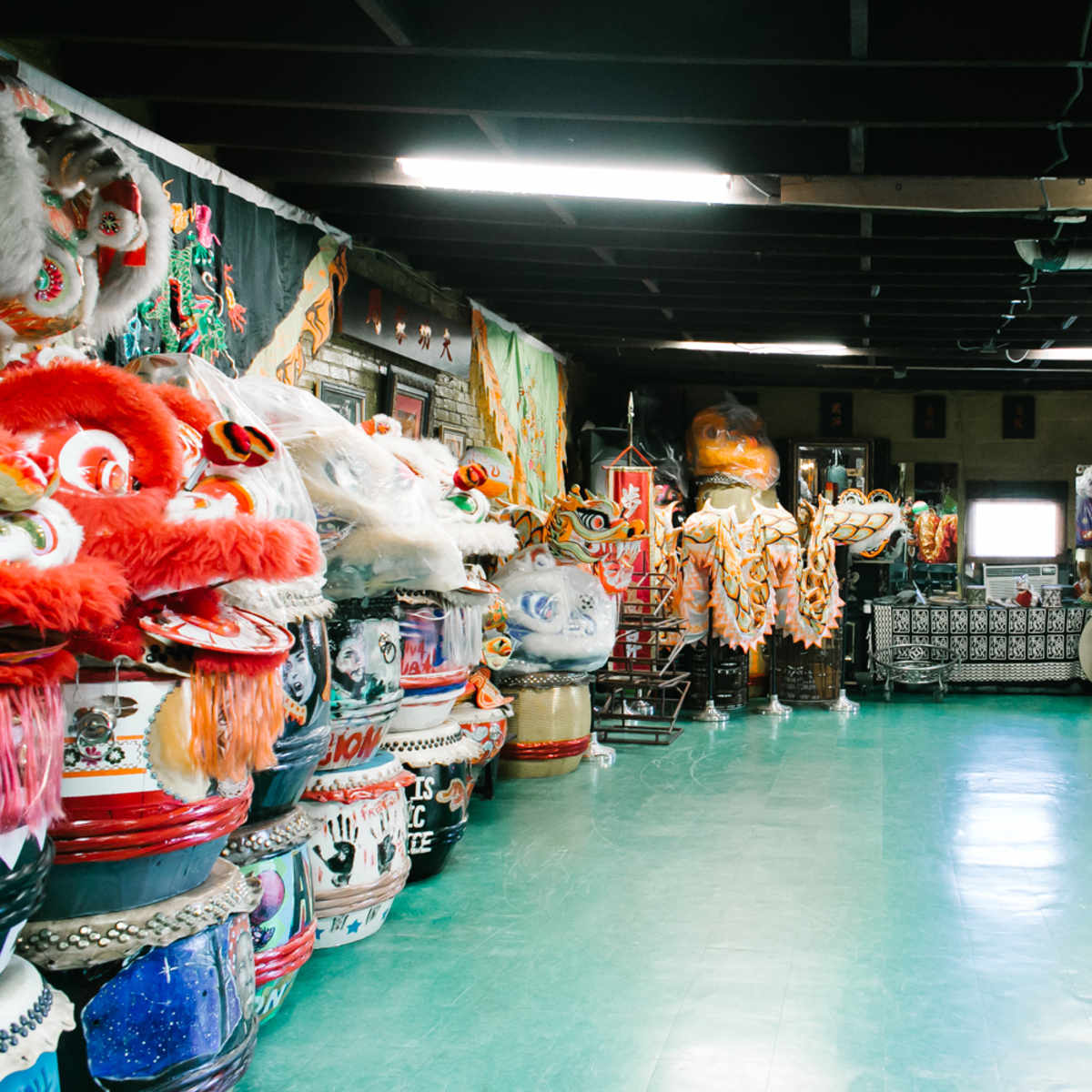 A spacious room filled with colorful traditional costumes, large lion dance heads, and various props lined along the walls.