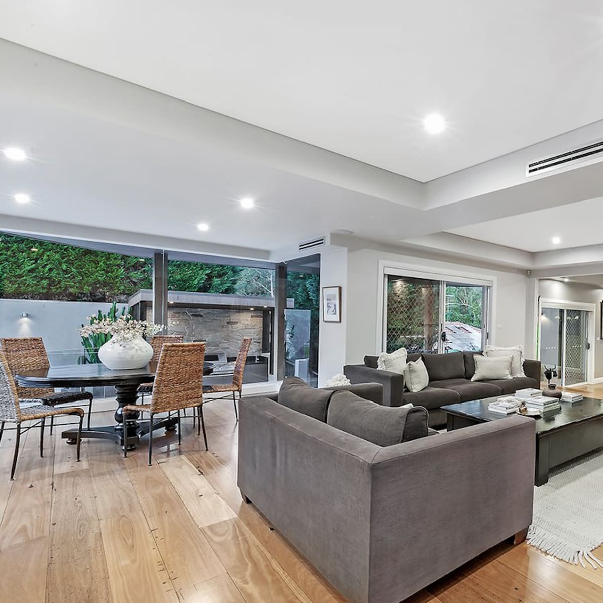 A spacious living room with a gray sofa, a stone fireplace, and a dining area featuring a glass table, all surrounded by wooden flooring.