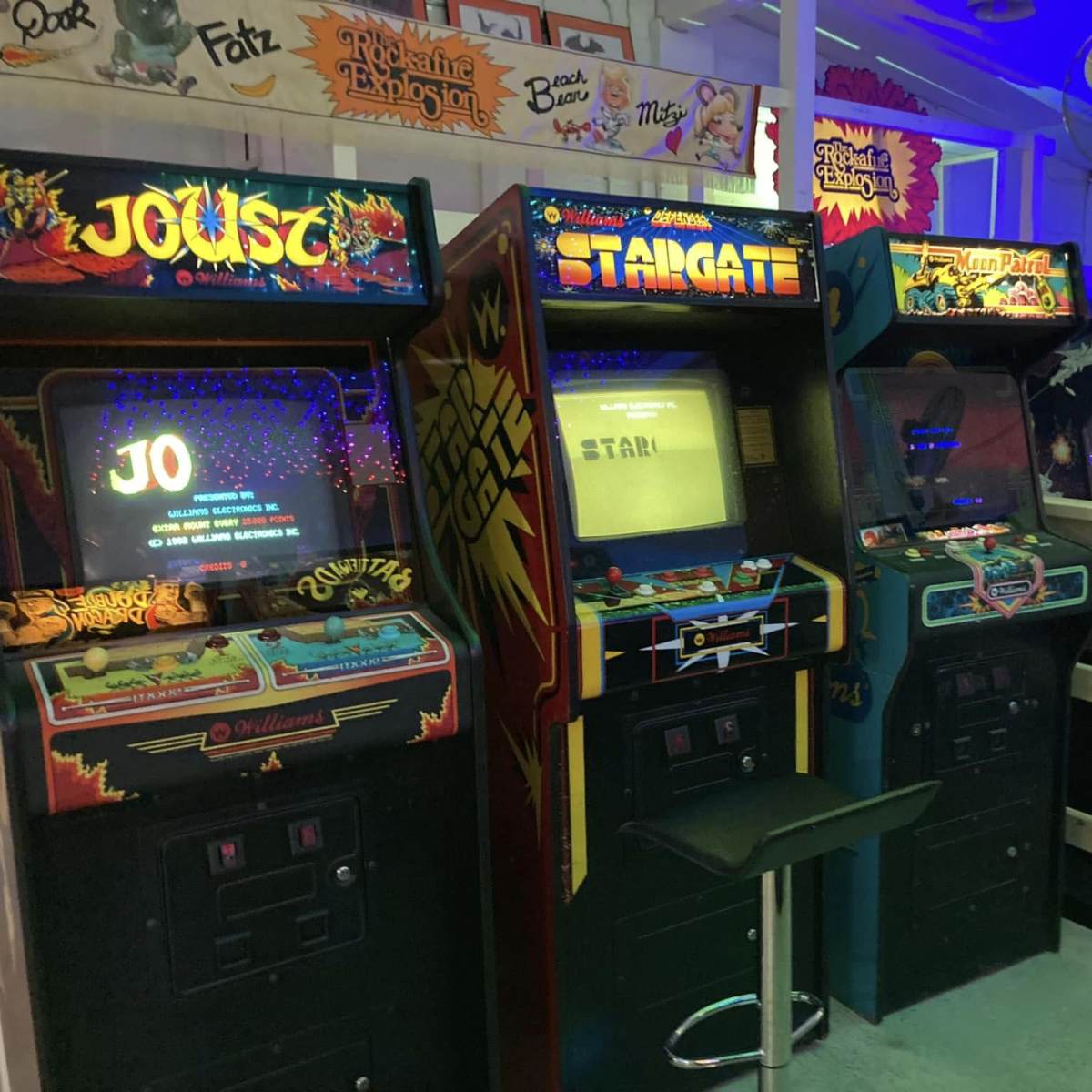 A row of classic arcade game machines, including "Joust," "Stargate," and "Pinball," in a retro gaming space.