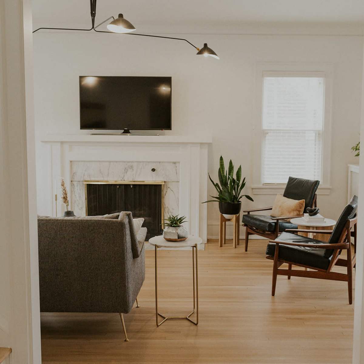 A modern living room features a gray sofa, a wooden chair, a marble fireplace, and a television mounted on the wall.