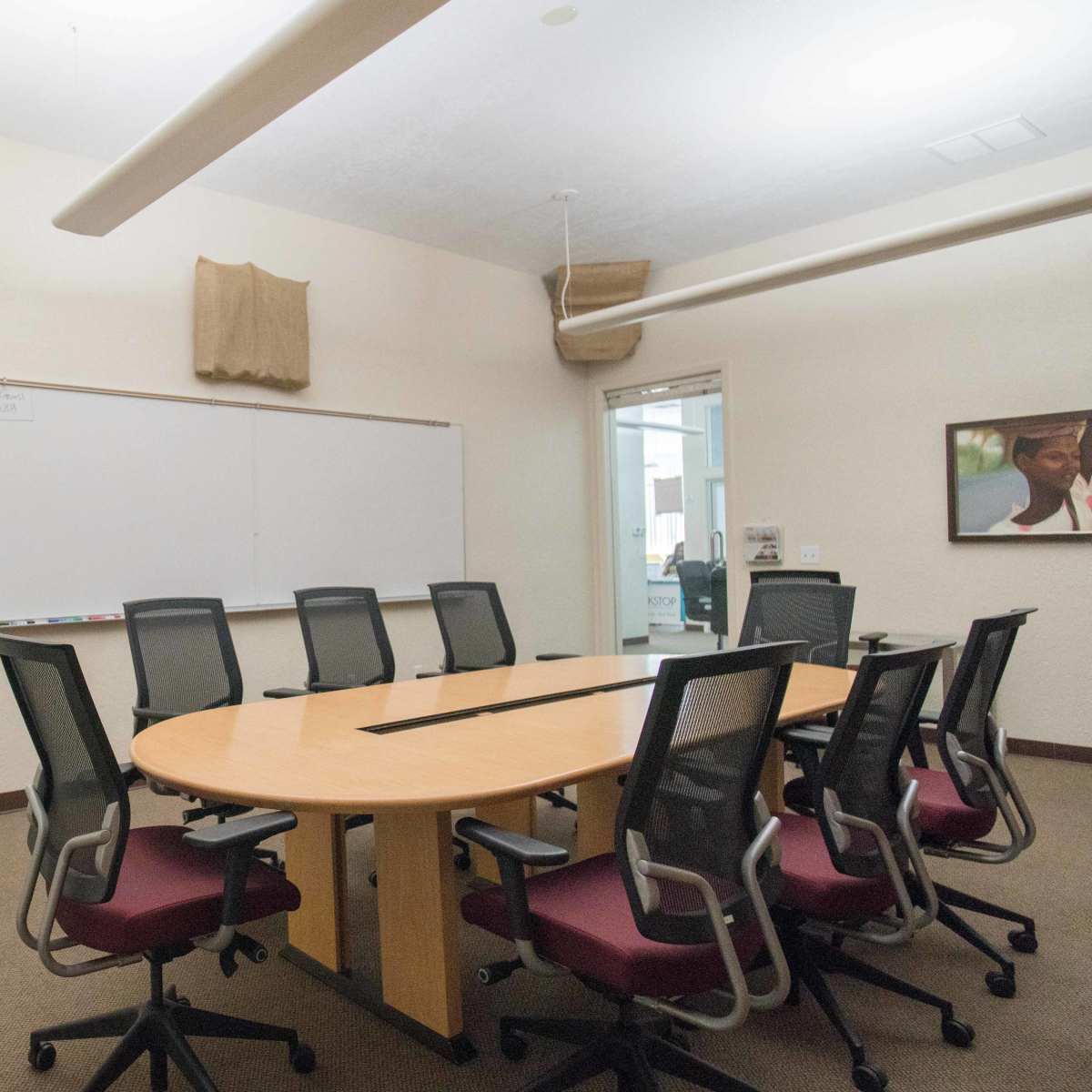 A conference room features a large circular table surrounded by rolling chairs, a wall-mounted television, and a whiteboard.