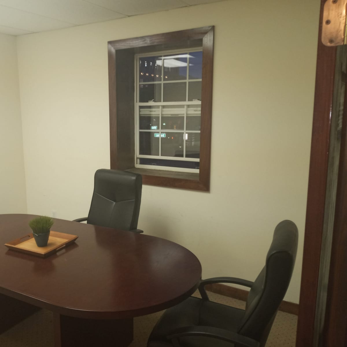 A small meeting room with a round table and three chairs, featuring a window that overlooks an outdoor scene at night.