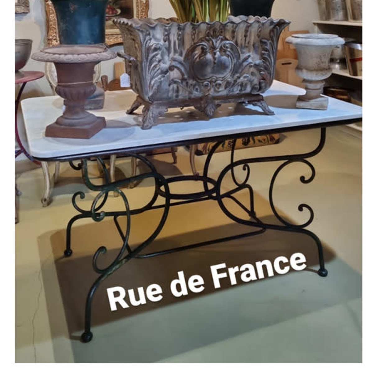 A decorative table displays a vintage planter with flowers, surrounded by various pottery and framed artworks in a shop labeled "Rue de France."