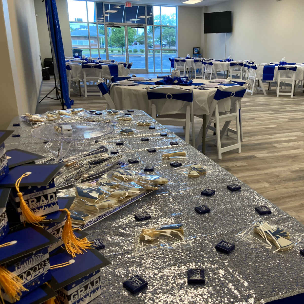 A decorated event space with tables set for a graduation celebration, featuring blue and silver decor and a display of graduation caps.