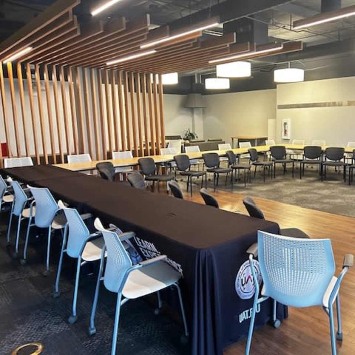 A spacious meeting room features a long table at the front and multiple rows of seating arranged in a circular formation.