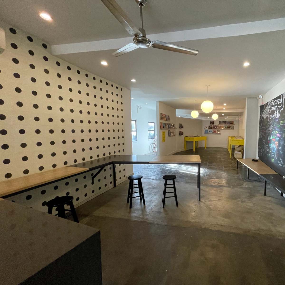 A modern, open space with two tables, high stools, a polka-dotted wall, and a chalkboard on one side.