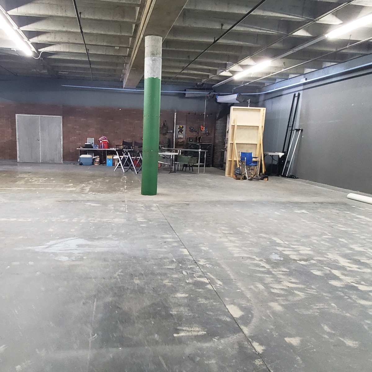 An empty industrial space with concrete flooring, green columns, and various tools and equipment arranged along the walls.