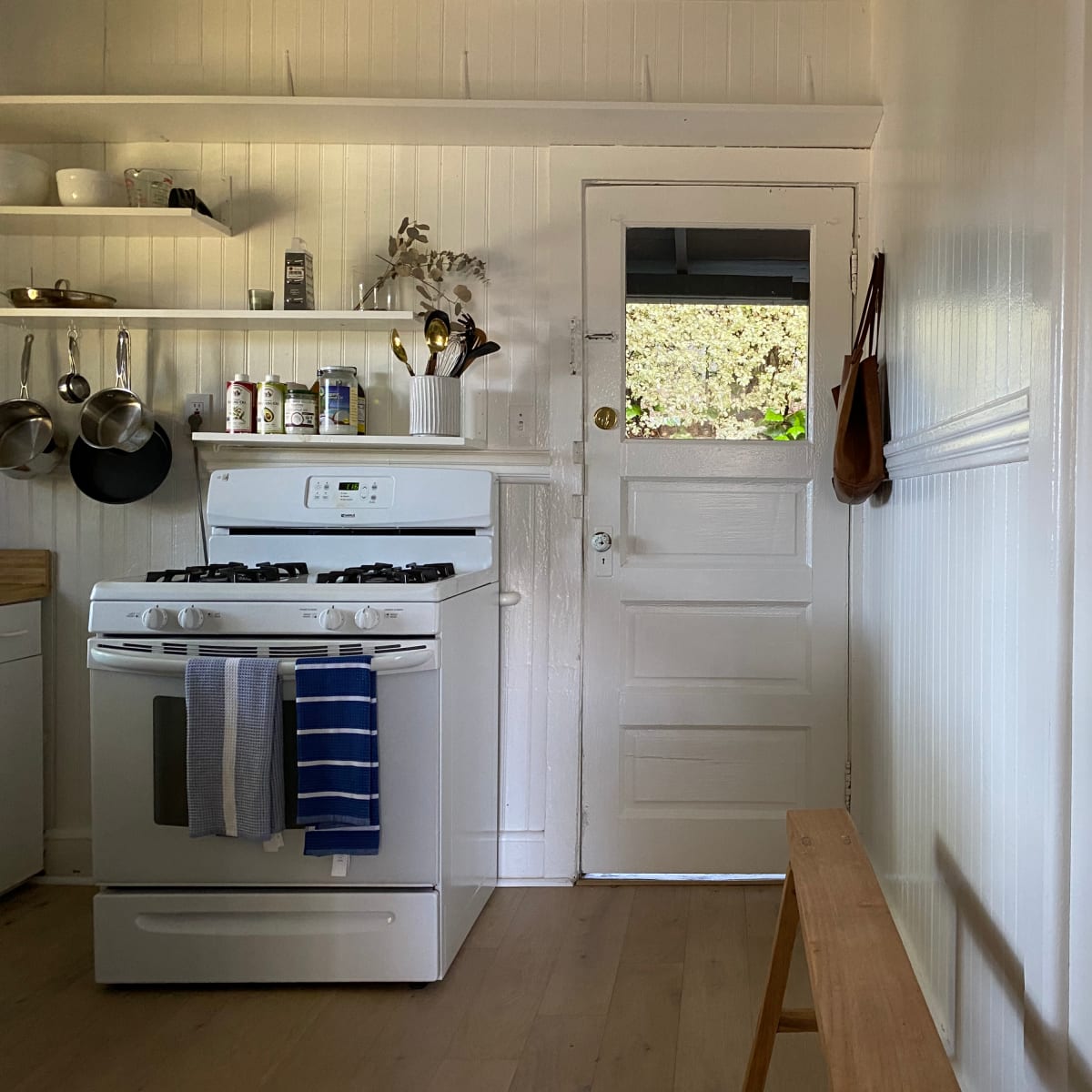 A clean kitchen features a white stove, shelves with kitchenware, and a door leading outside.