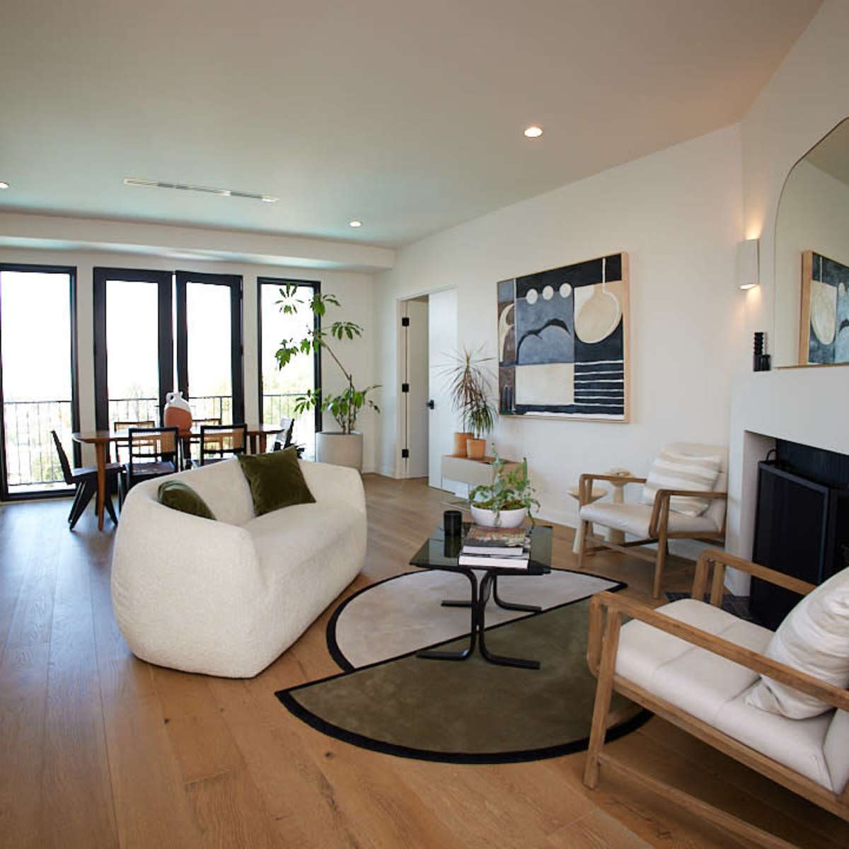 The spacious living room features a cozy white sofa, two armchairs, a round coffee table, and large windows that provide natural light.