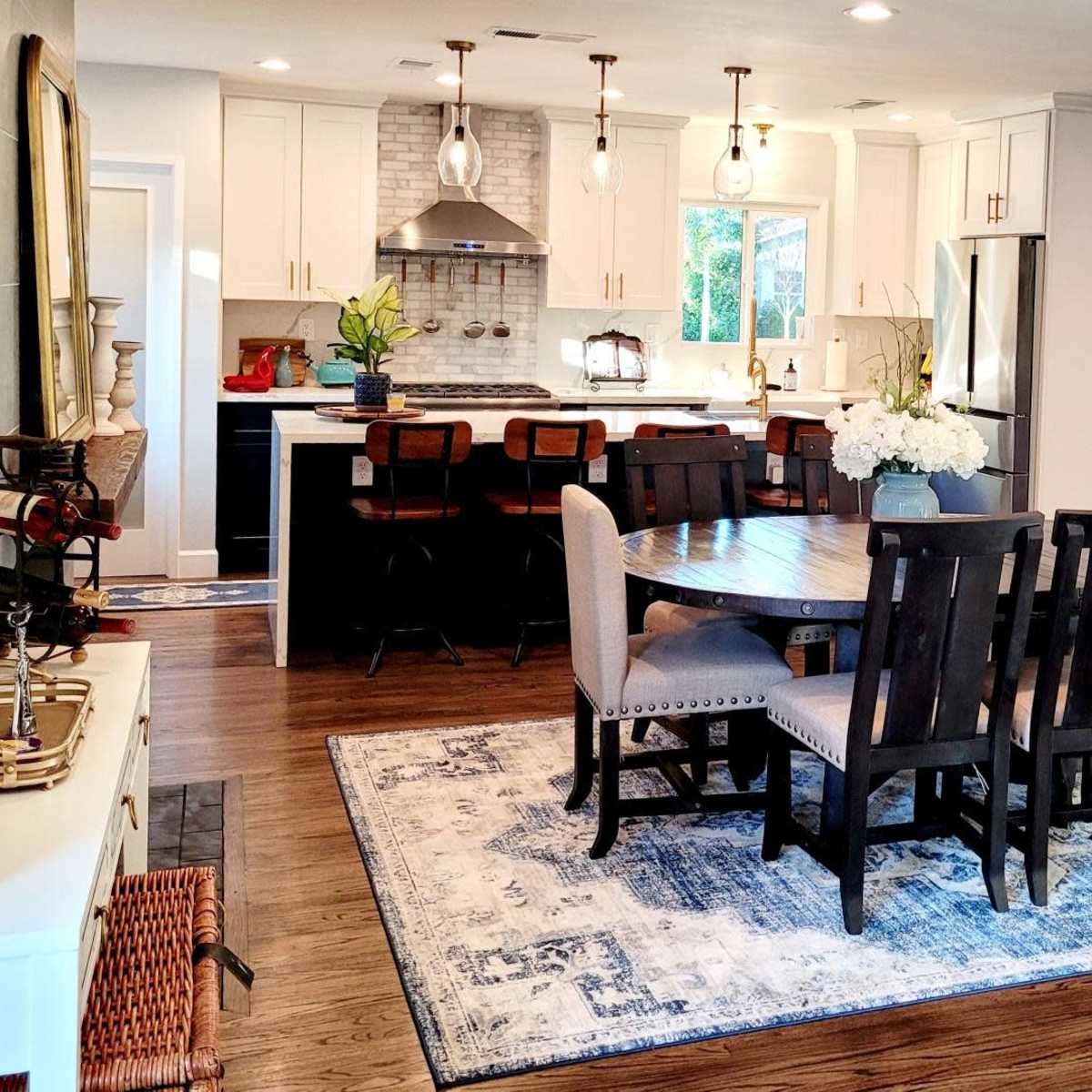 A modern kitchen and dining area featuring a round table surrounded by chairs, with a view of stylish cabinetry and appliances in the background.