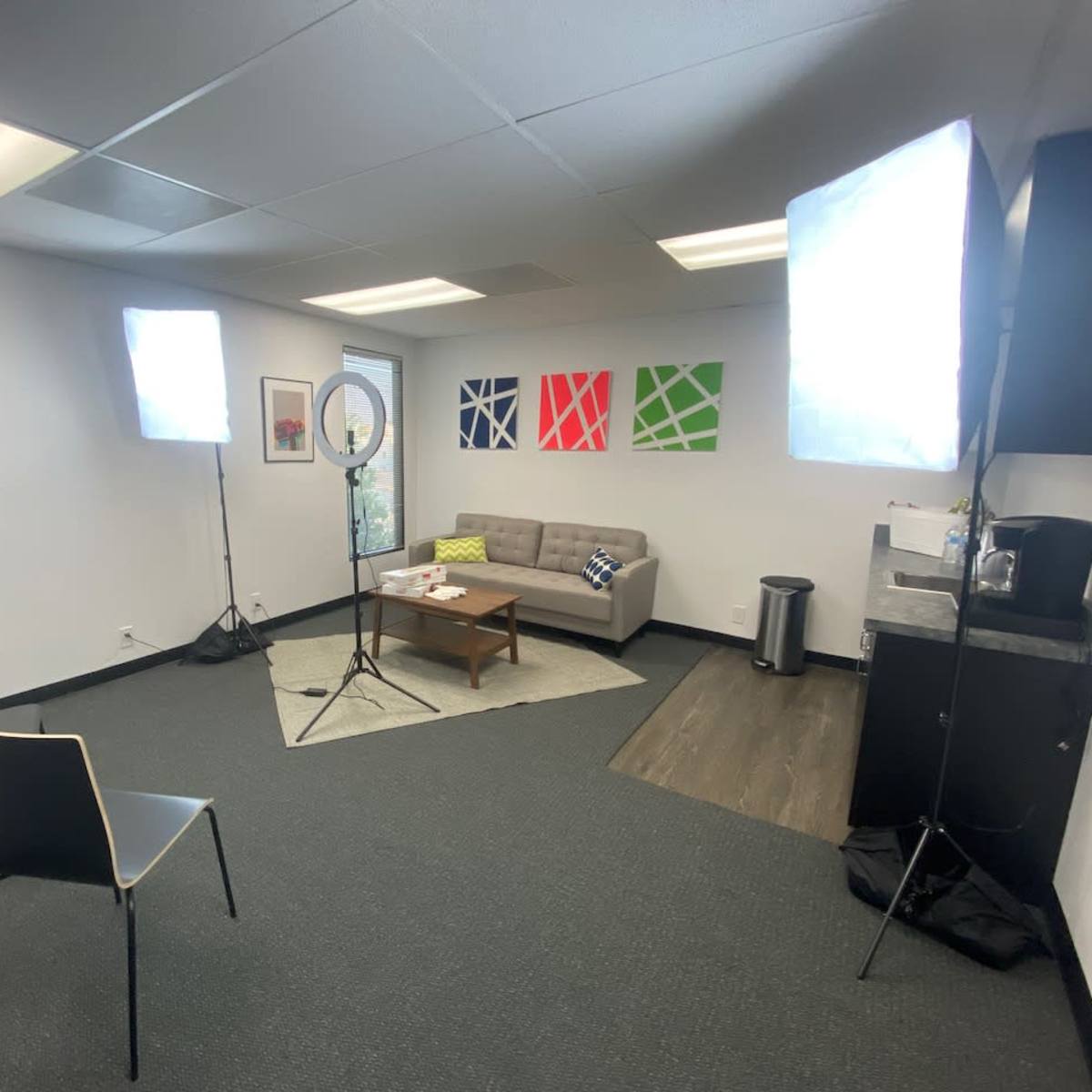 A well-lit office space with a gray couch, two chairs, and studio lighting setup around a small coffee table.