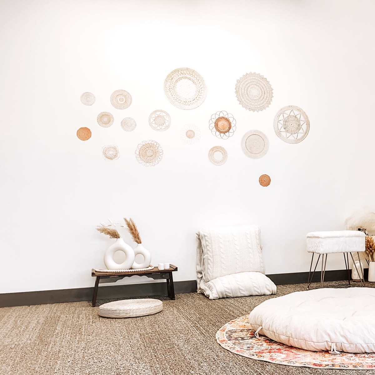 A minimalist interior with a large mirror, decorative wall art, a circular floor cushion, and soft furnishings arranged in an open space.