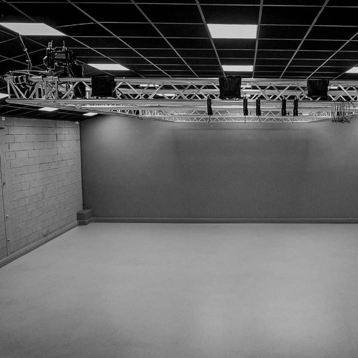 An empty studio space with a grid ceiling and a lighting rig suspended above.