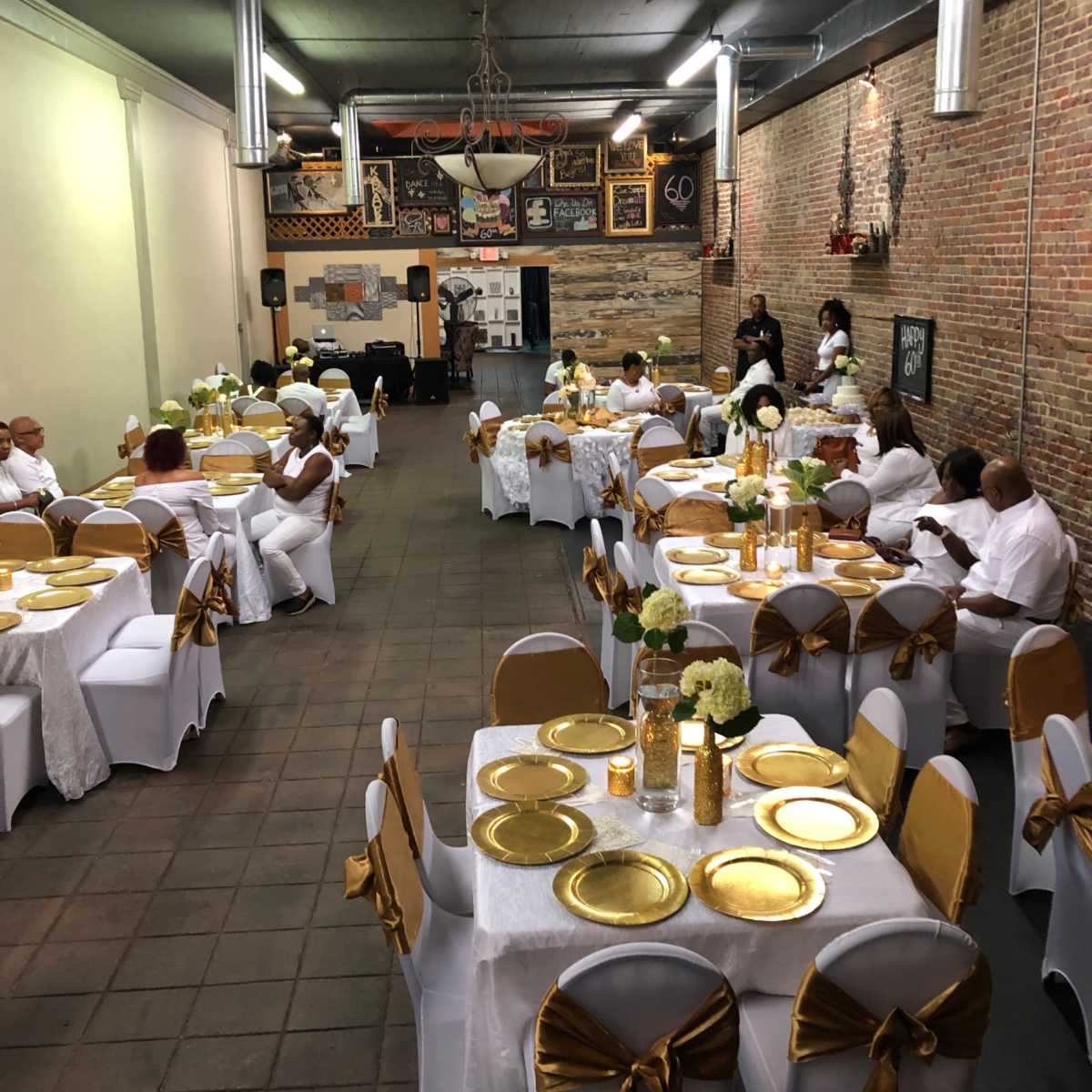 A spacious event hall set for a formal gathering, featuring tables adorned with white and gold decorations.