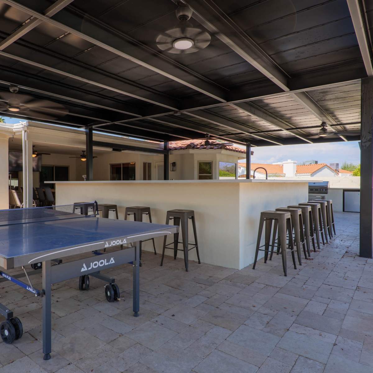 A covered outdoor area featuring a ping pong table and a bar with several stools.