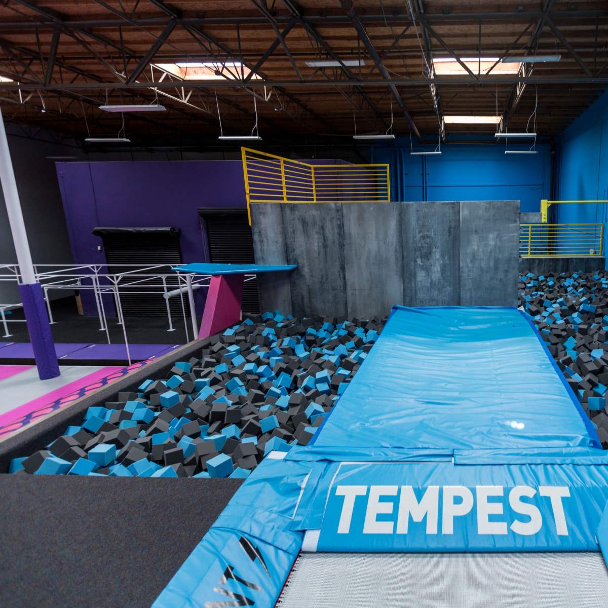 A trampoline park with a landing area filled with black foam blocks and a blue mat labeled "TEMPEST."