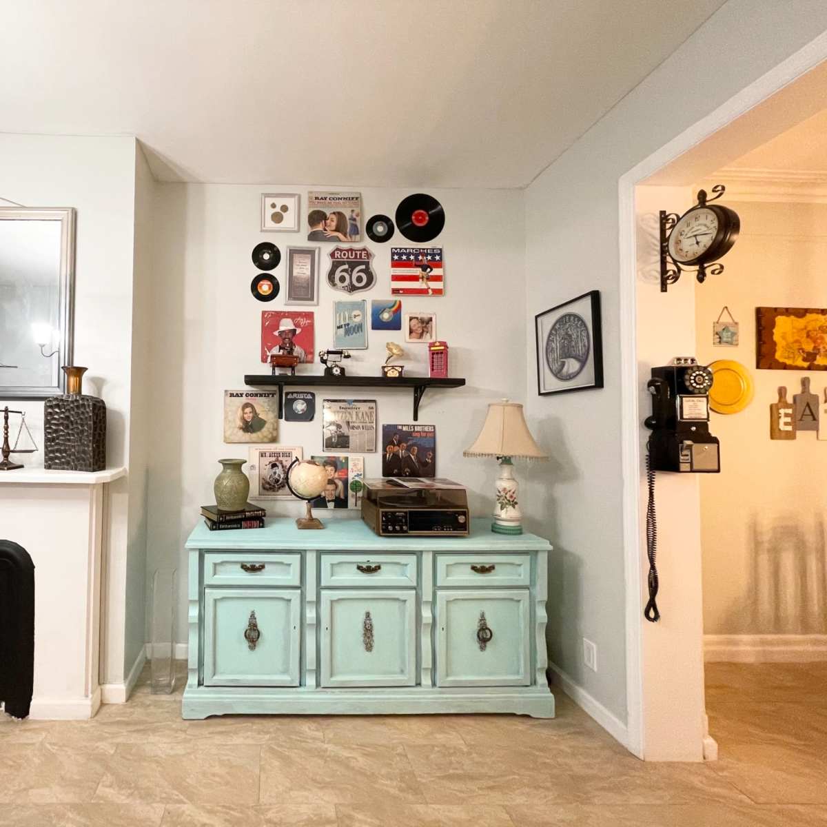 A living room with a light-colored wall featuring a vintage record and memorabilia display above a blue sideboard, while a vintage telephone hangs on the adjacent wall.