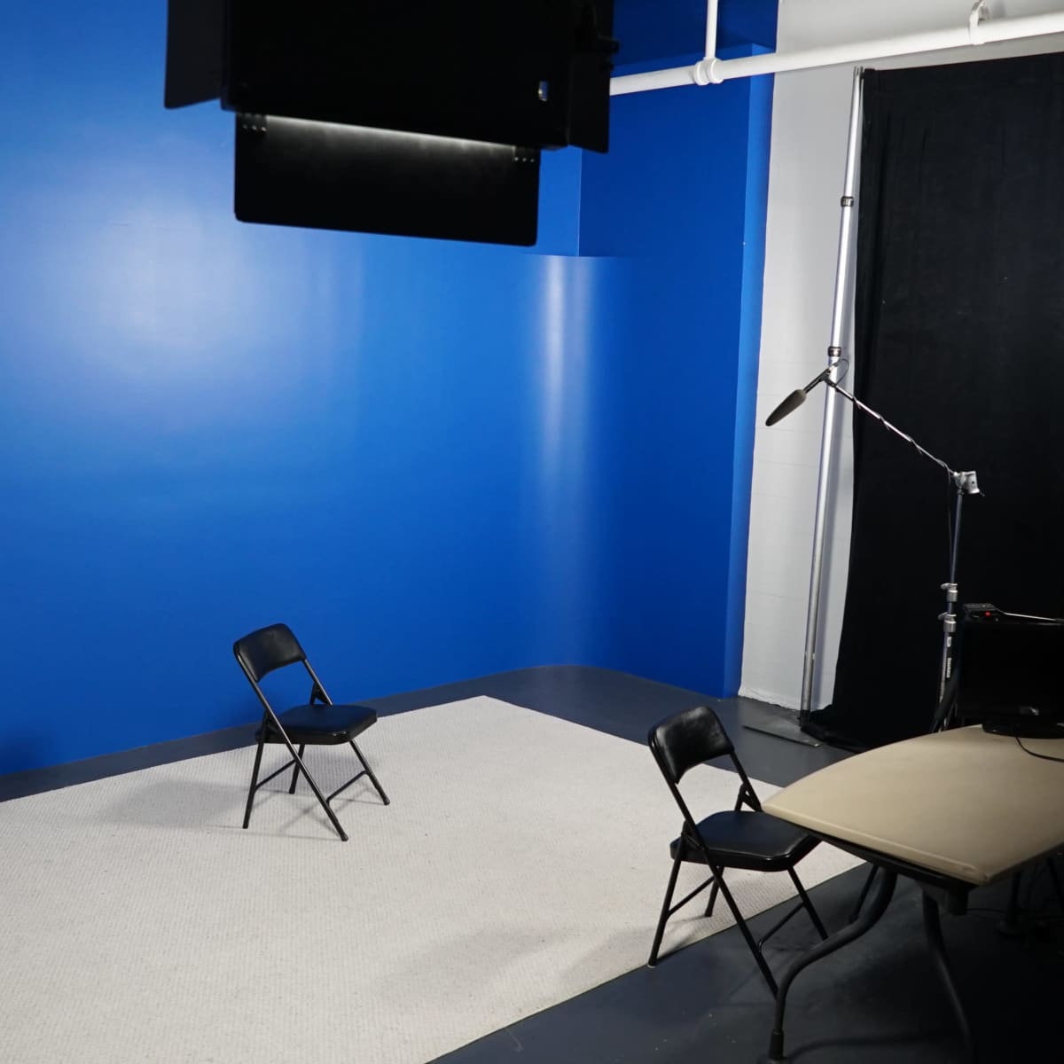 An empty studio space with a blue wall, two black chairs, and a table under soft lighting.