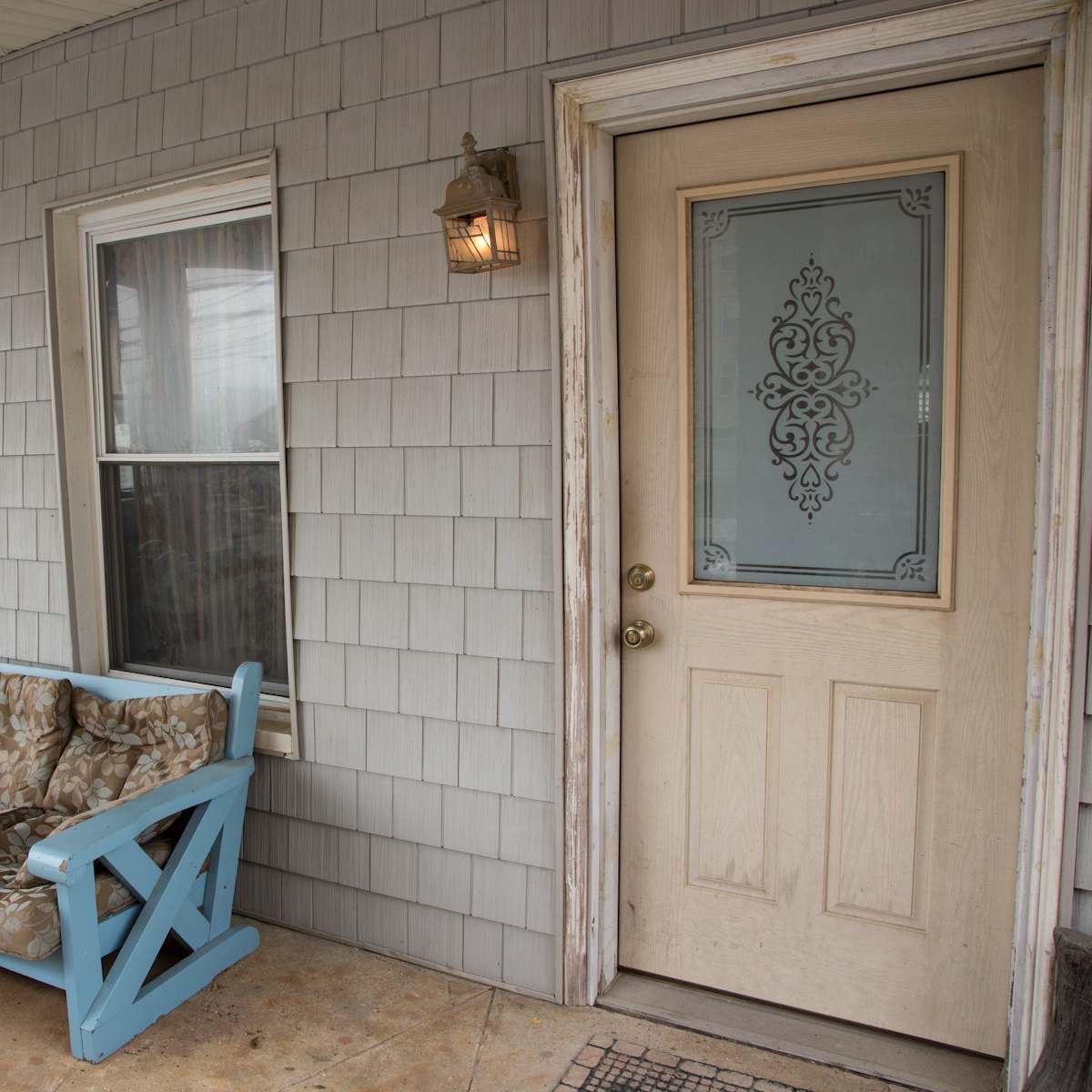 A porch with a light blue couch and a matching small table, situated in front of a door with decorative glass elements.