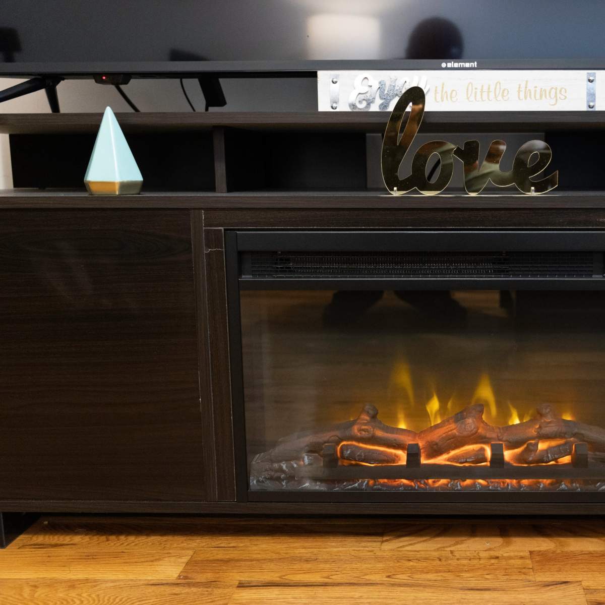 A television unit with an electric fireplace and a decorative sign that reads "love" on top.