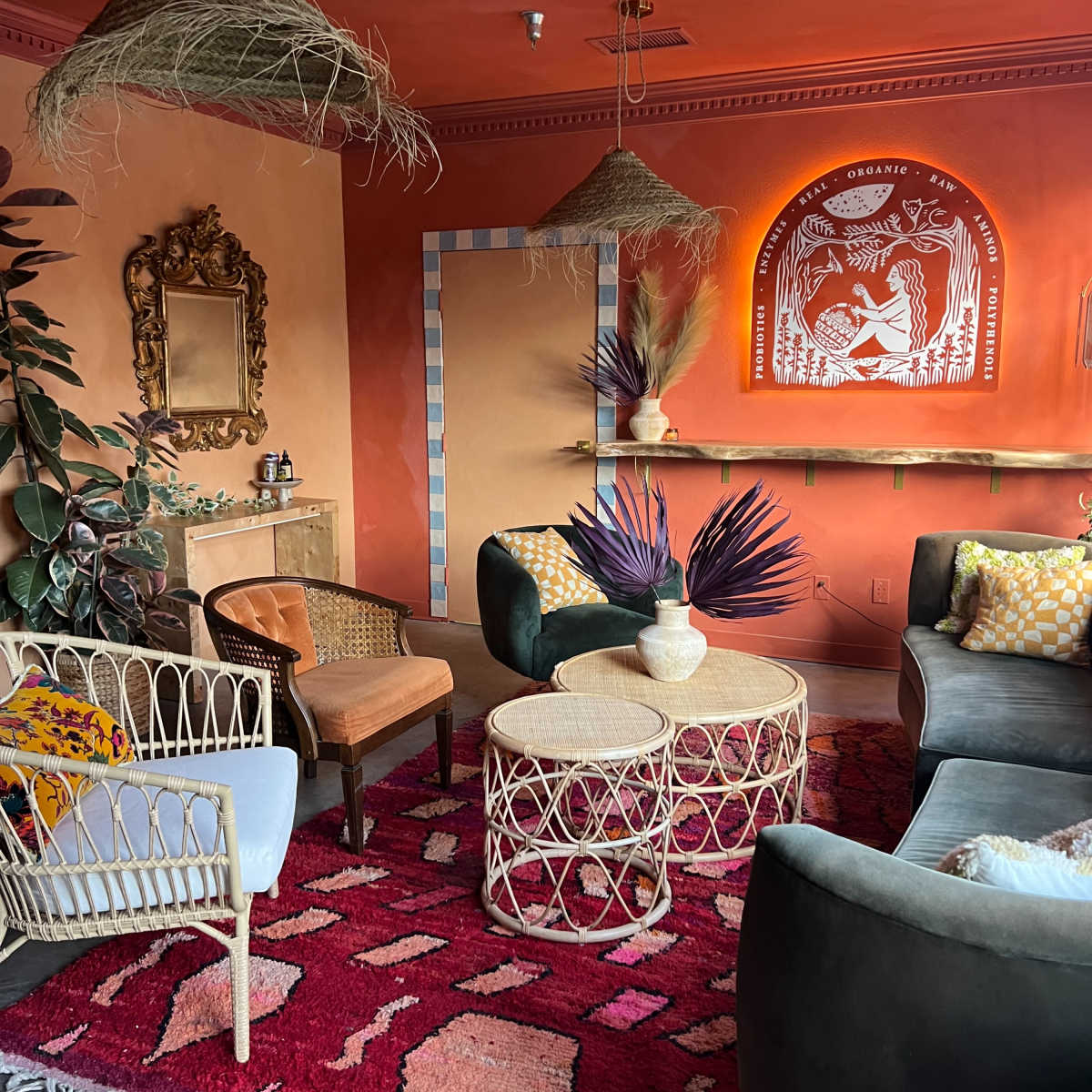 The scene depicts a cozy indoor lounge featuring earthy-toned walls, eclectic seating arrangements, decorative lighting, and vibrant textile accents.