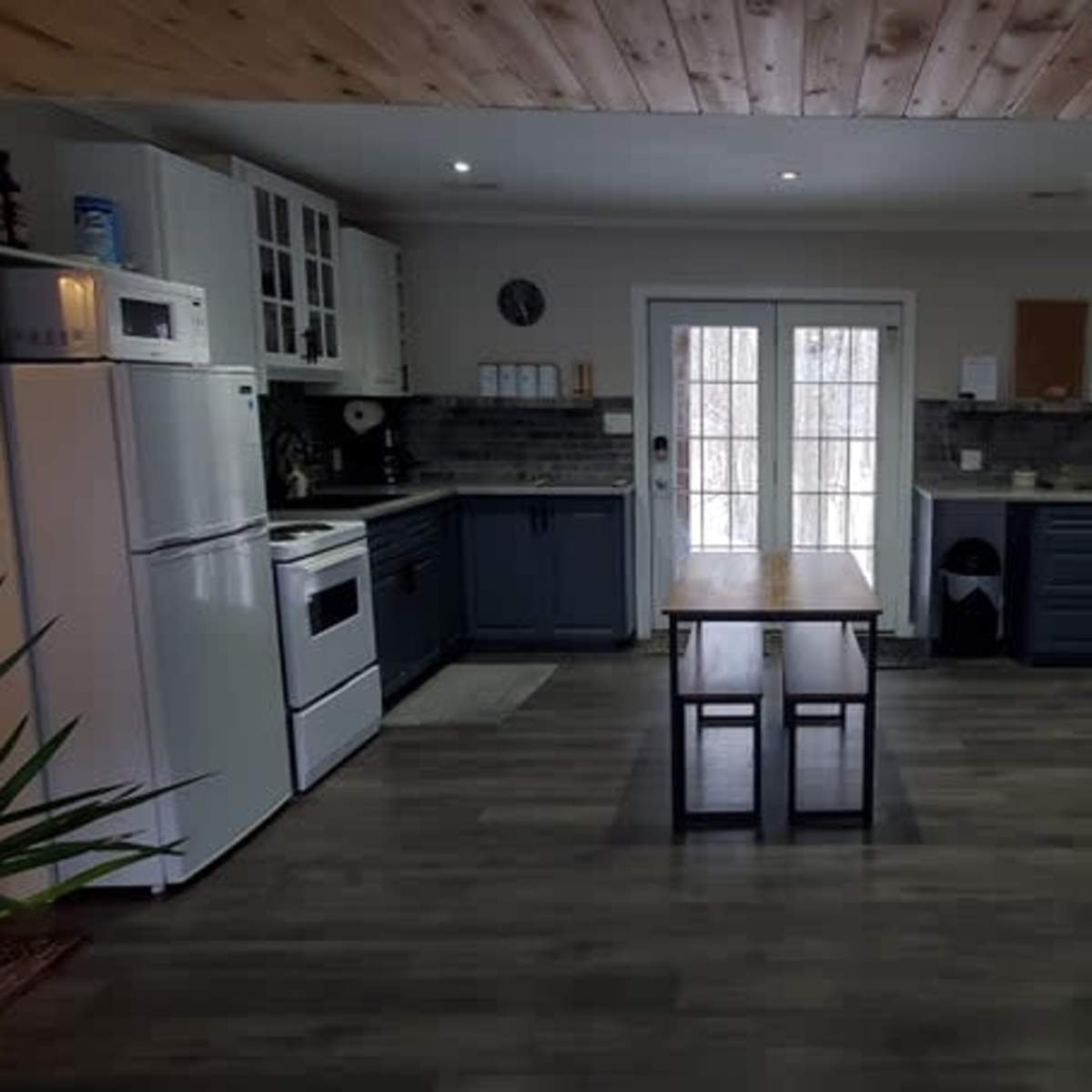 A spacious kitchen features a central table, white cabinets, a dark stove, and large windows leading to an outdoor area.