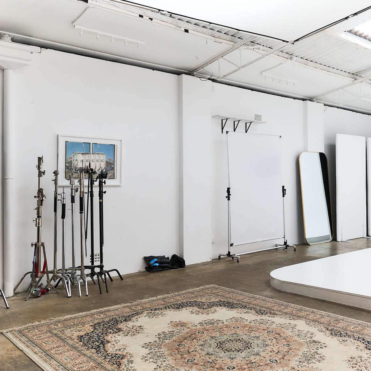 A spacious photography studio with various equipment, including light stands and blank backdrops, alongside a decorative rug on the floor.