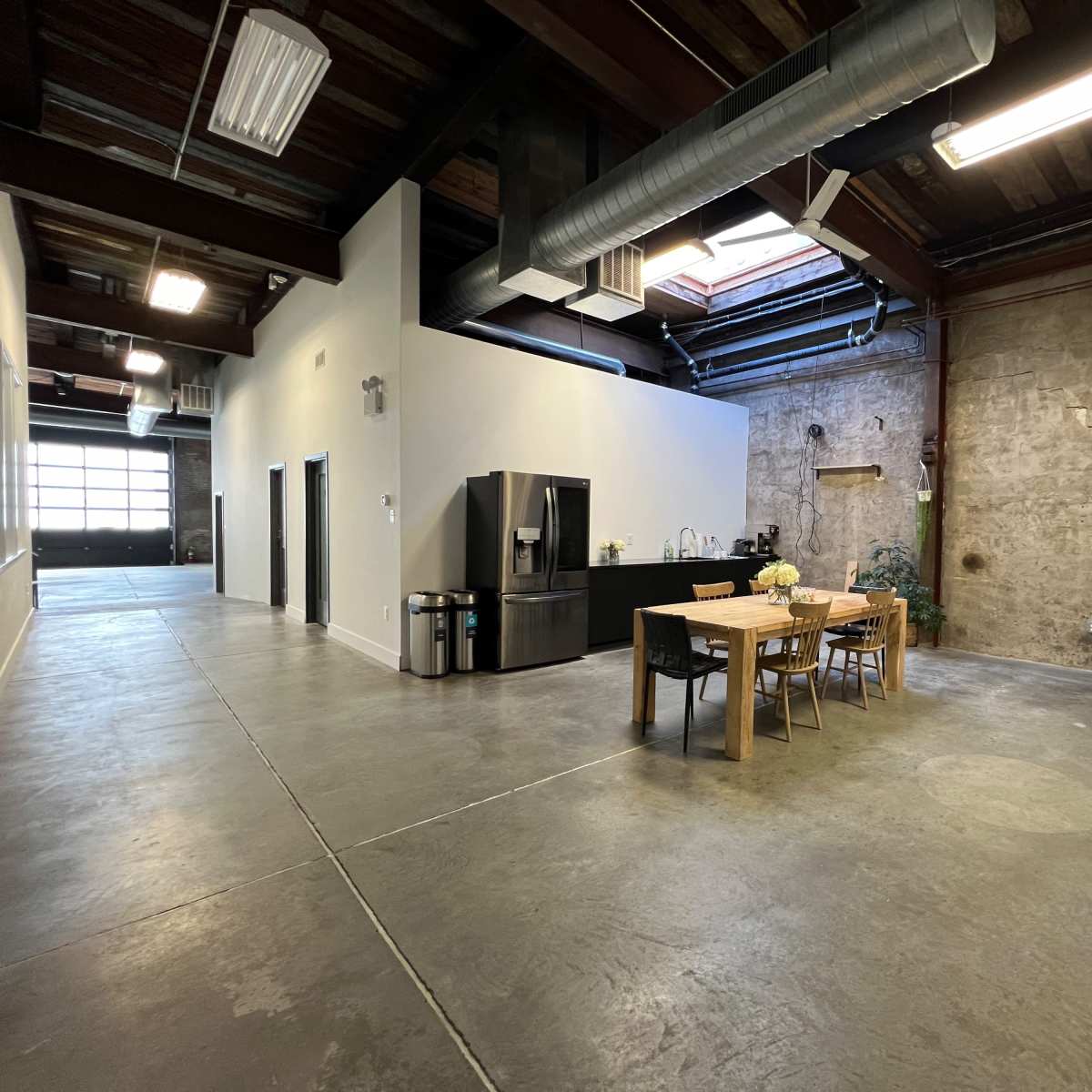 A spacious interior with a dining table and chairs set against a textured stone wall, while a kitchen area with a refrigerator is visible on the left side.