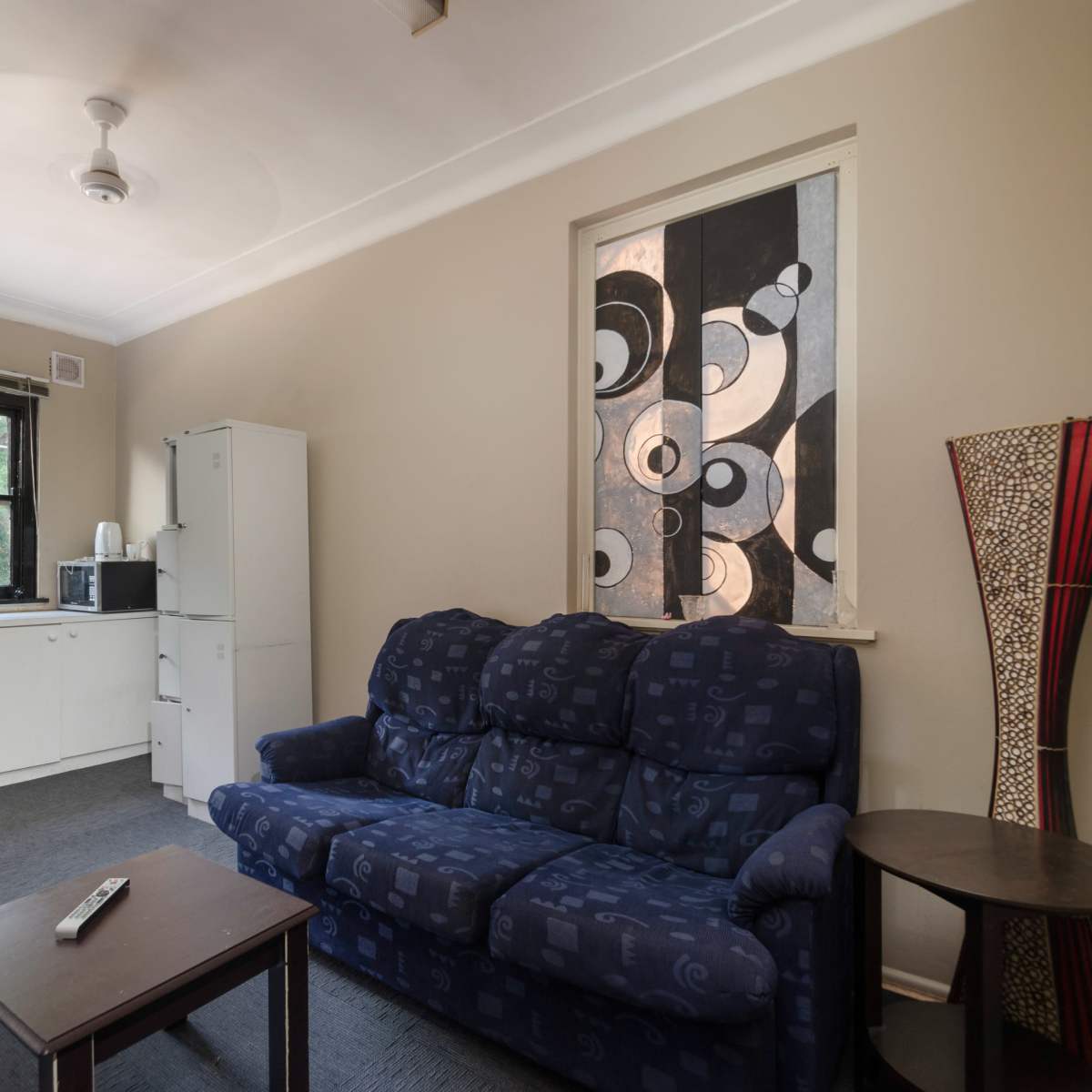 A small living area with a blue sofa, a wooden coffee table, and a kitchenette in the background.