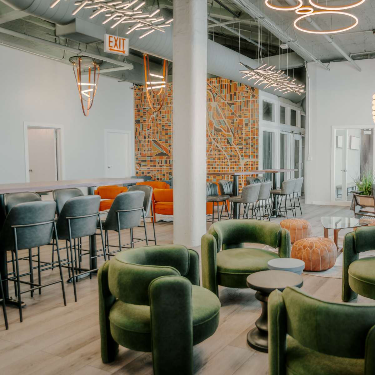 A modern lounge area featuring green armchairs, a mix of seating options, a patterned accent wall, and large windows.