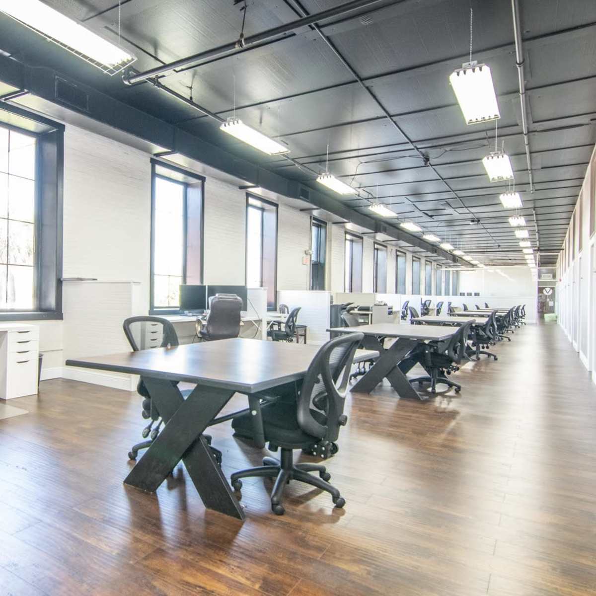 A spacious, modern office with a row of desks and ergonomic chairs arranged along a well-lit corridor.