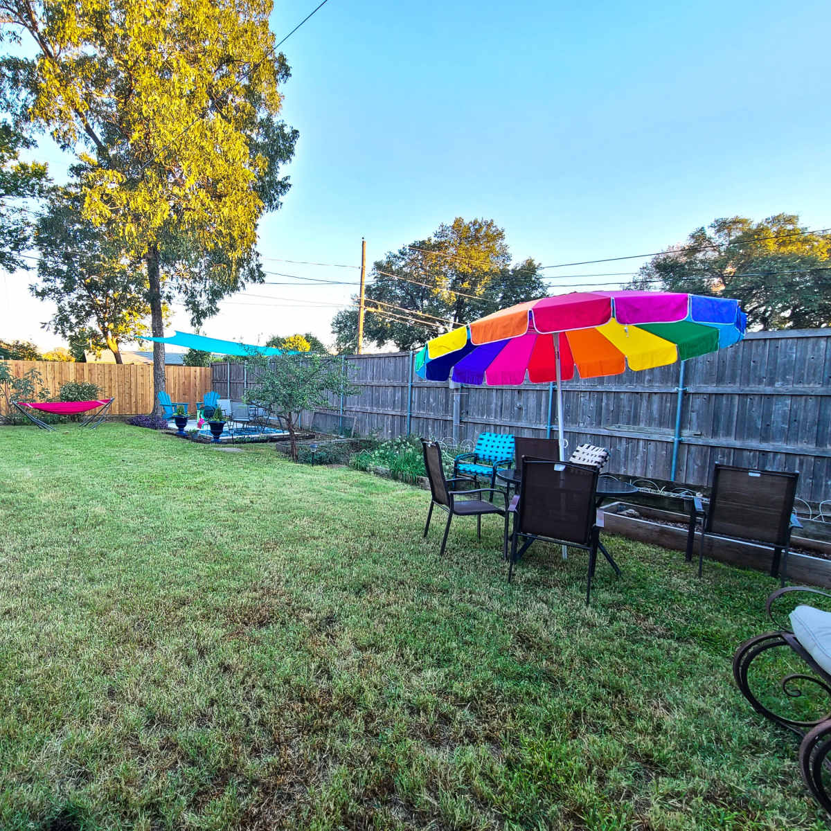 A grassy backyard with seating areas, colorful umbrellas, and trees in the background.