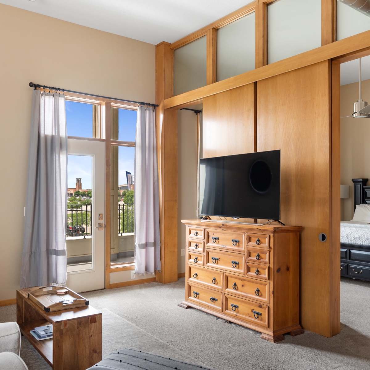 A modern living space with a comfortable seating area, a wooden dresser, and a television, separated from a bedroom by a wooden partition.