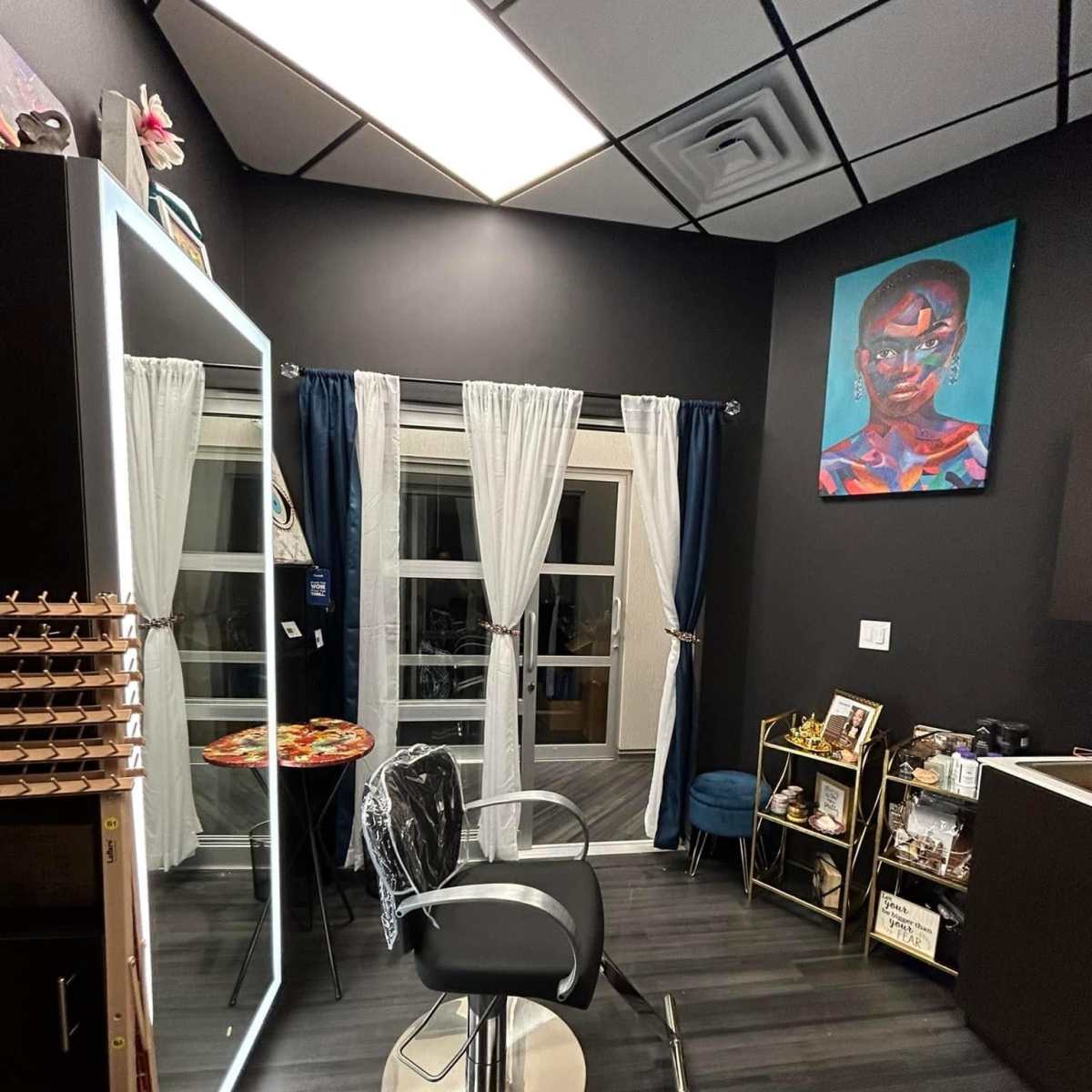 A small, modern salon interior with a styling chair, a large mirror, and artwork on the walls.