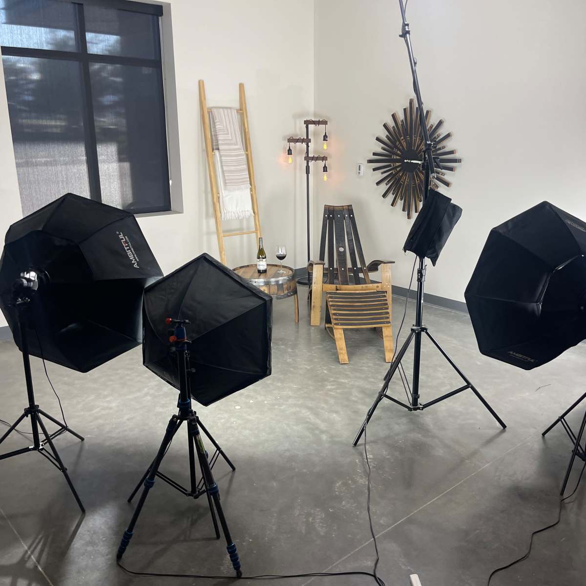 A well-lit photography studio setup featuring multiple softbox lights positioned around a wooden chair and decorative wall elements.