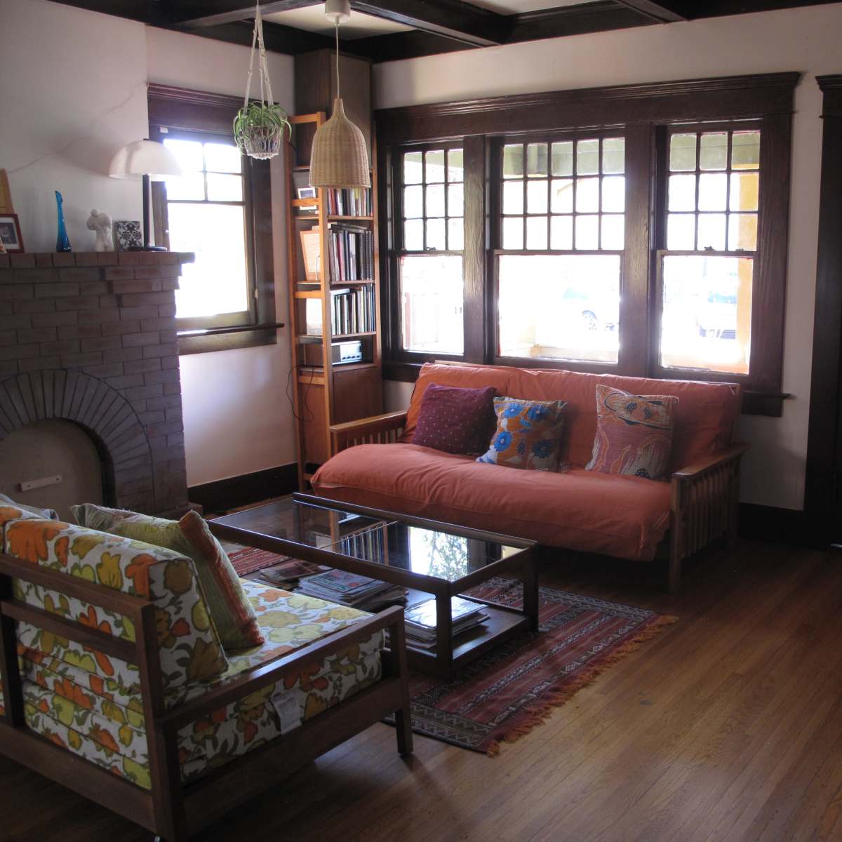 A living room featuring a sofa and armchair, a coffee table, a fireplace, and large windows with stained glass.