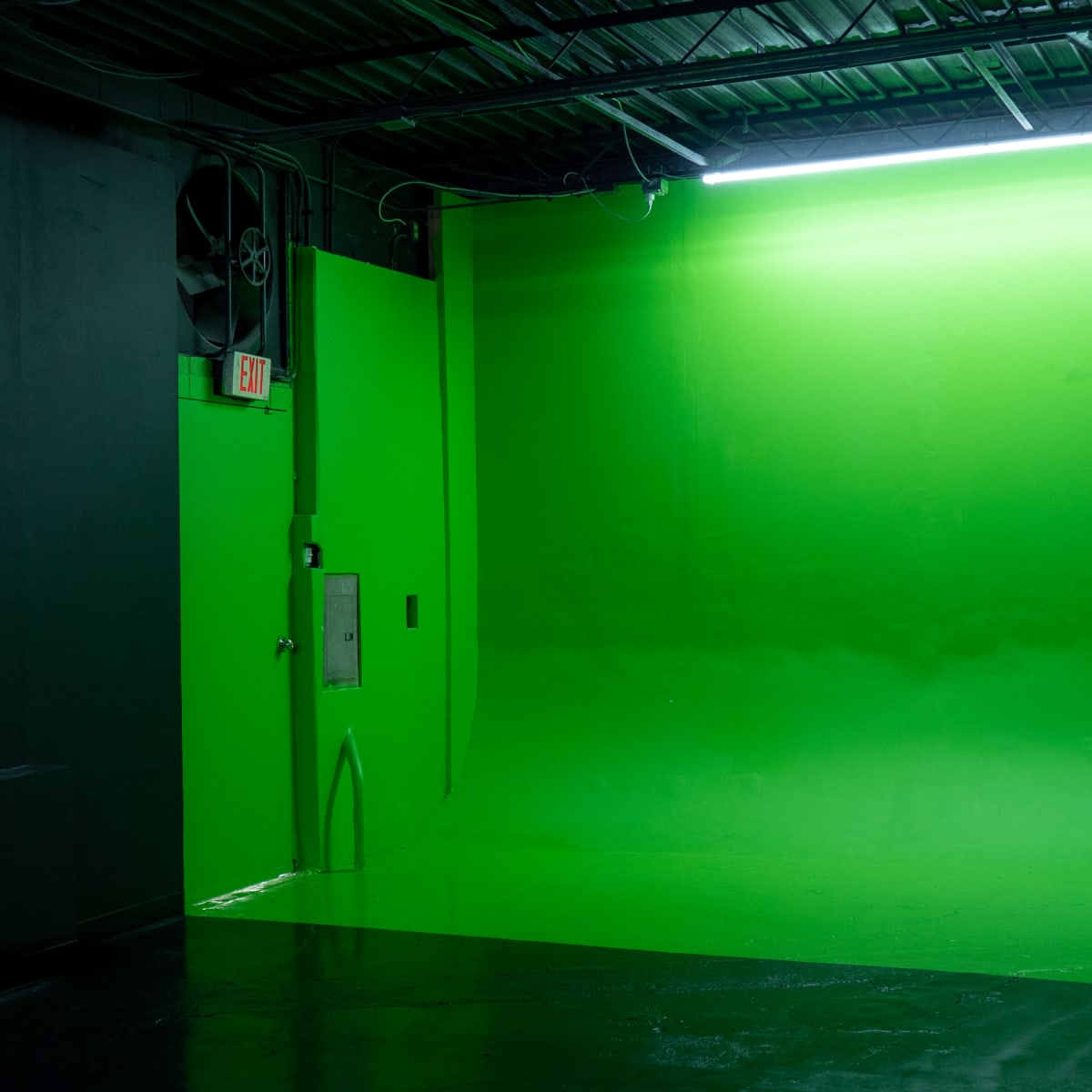 An empty room with a large green backdrop and dark walls.