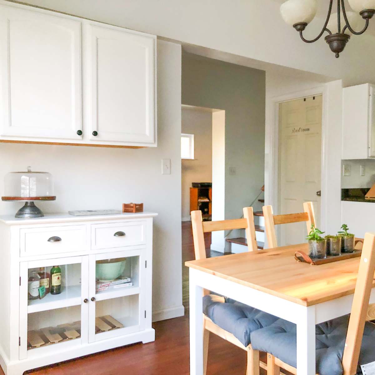 A bright kitchen and dining area featuring a wooden table with chairs, a white cabinet, and modern appliances.