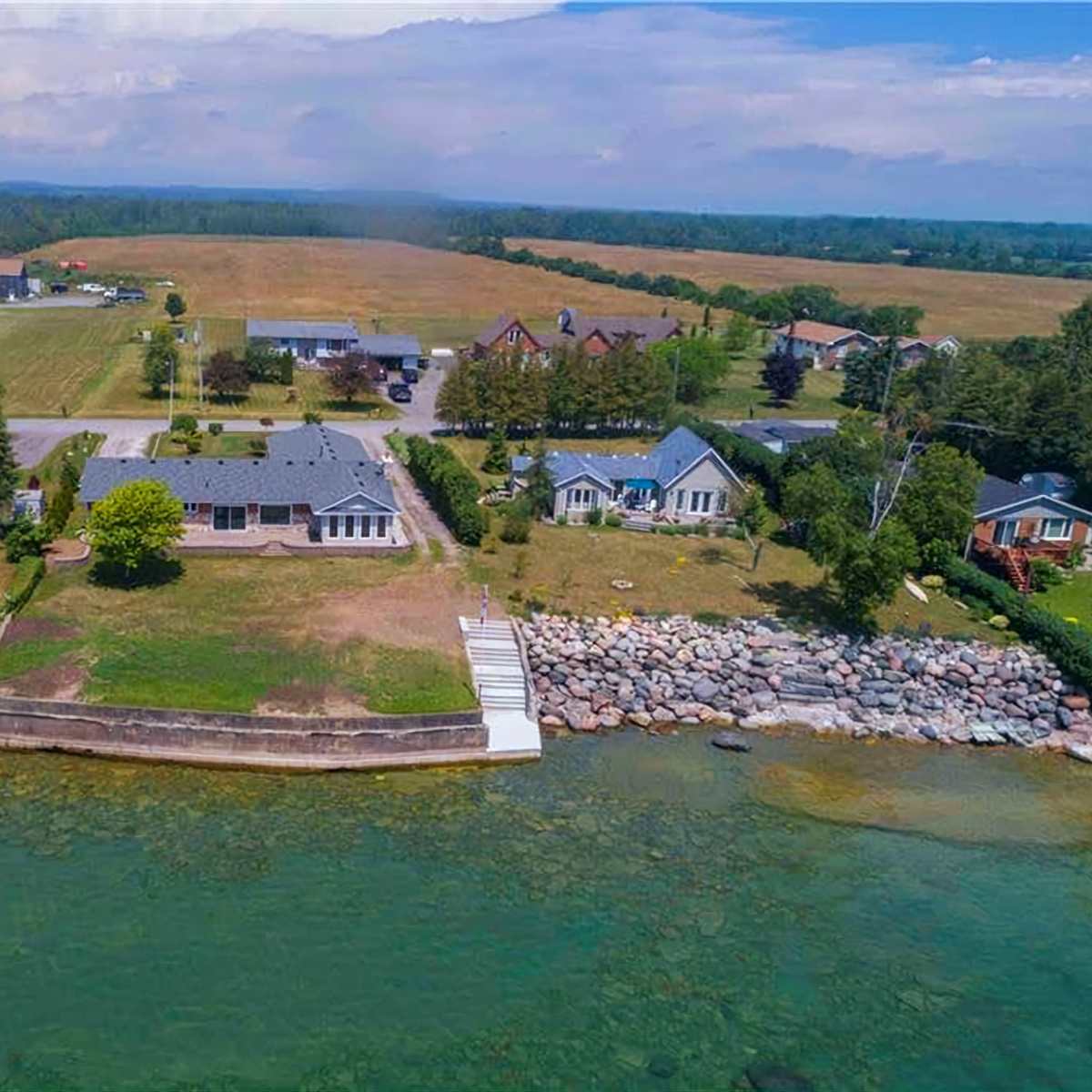 A waterfront property with a house and a landscaped yard, surrounded by fields and several nearby buildings.