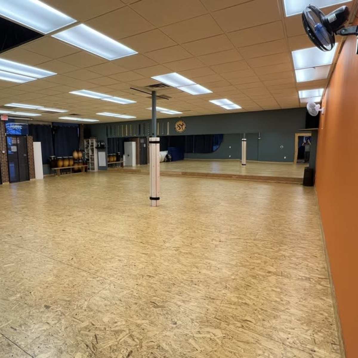 A spacious dance studio with wooden flooring, mirrors on one wall, and various equipment neatly arranged along the sides.