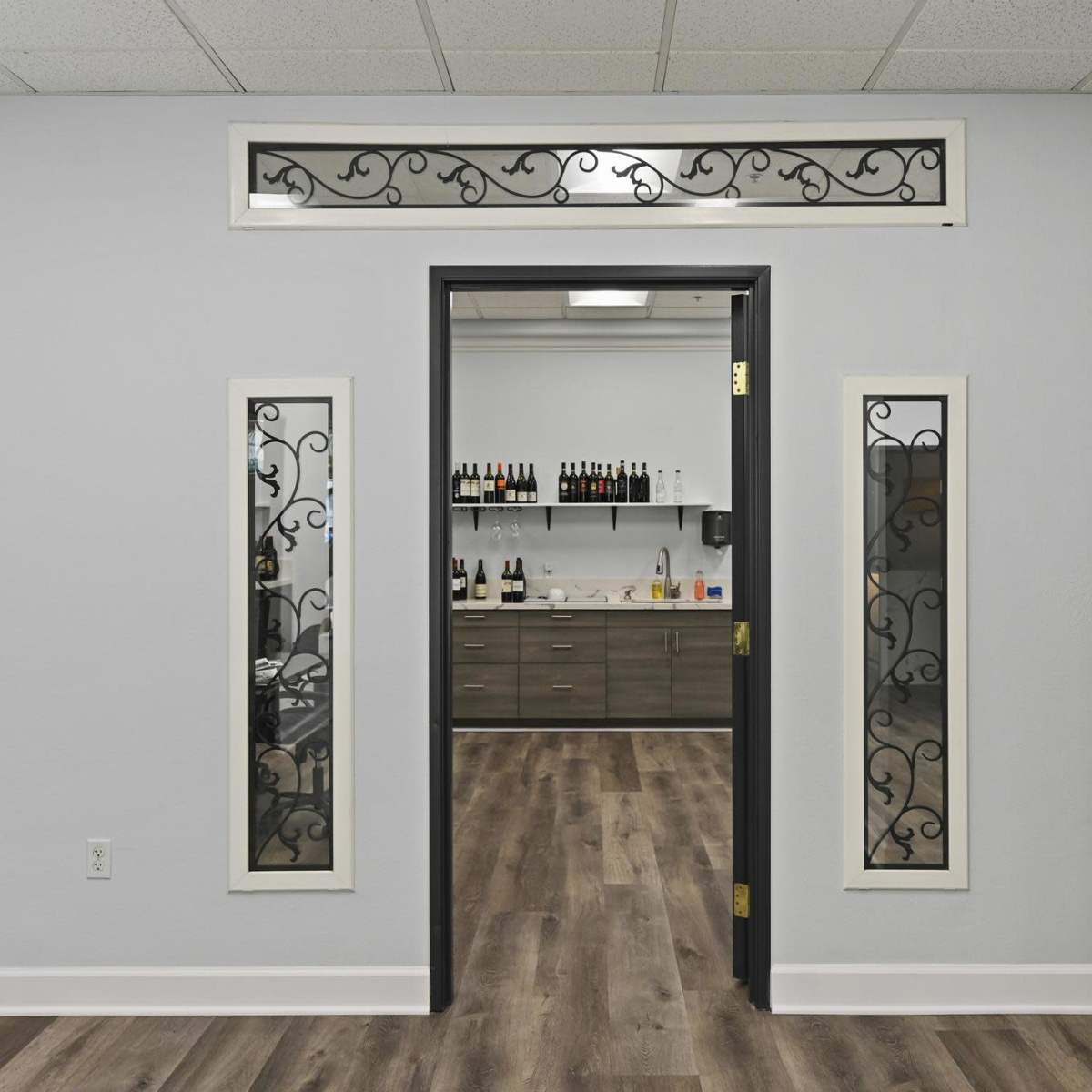 A clean interior space featuring a doorway with decorative panels and a well-organized room behind it, containing shelves with bottles and cabinetry.