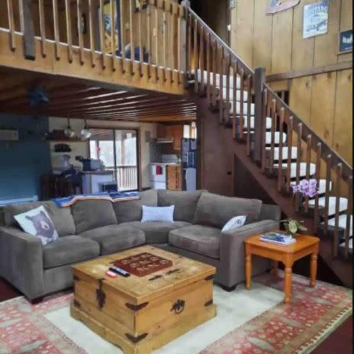 A cozy living room with a gray sectional sofa, a wooden coffee table, and a staircase leading to an upper level.