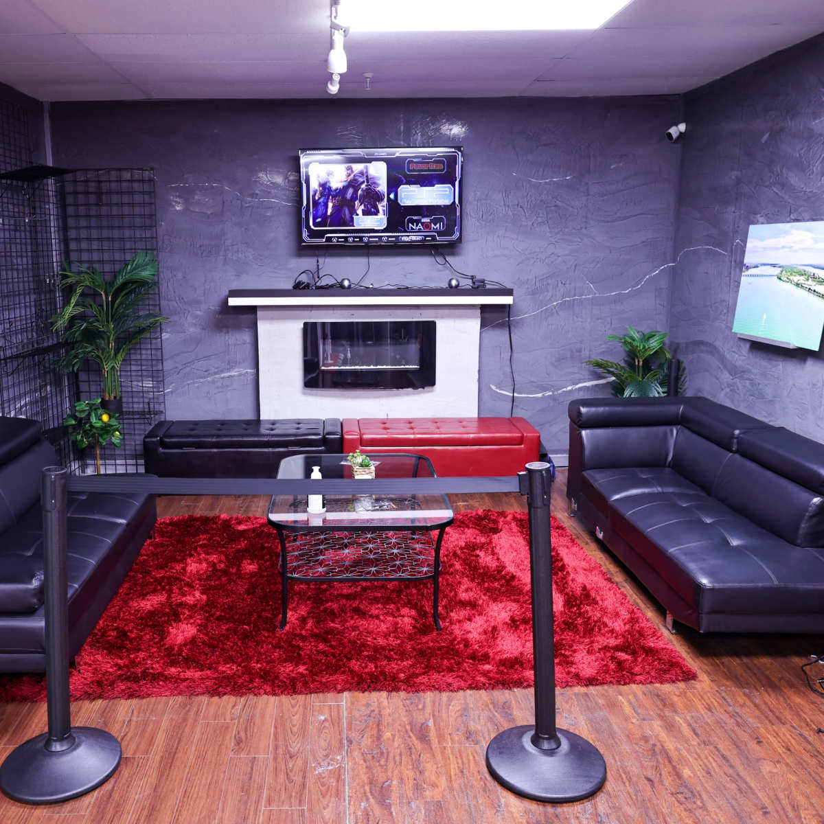 A modern lounge area with two black sofas, a red rug, a coffee table, and a wall-mounted television above a white fireplace.