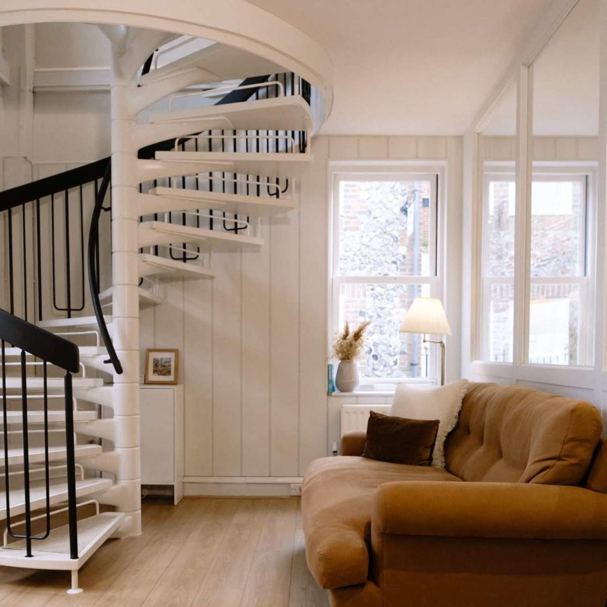 A cozy living area featuring a brown couch, a spiral staircase, and a window with natural light.
