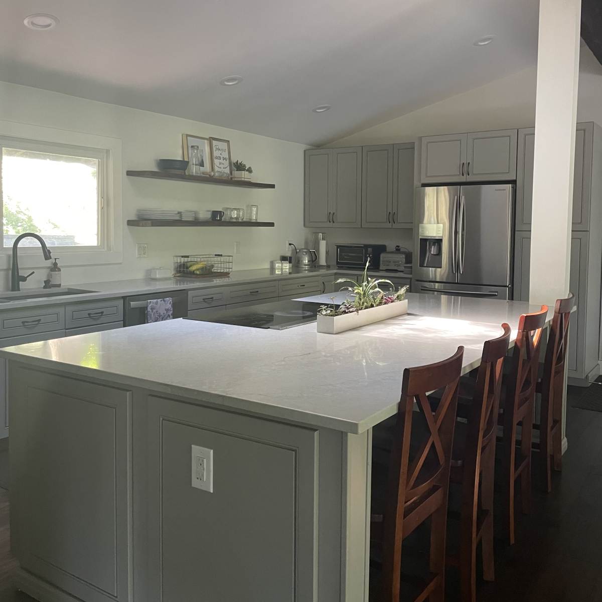The kitchen features gray cabinets, a central island with bar seating, stainless steel appliances, and a skylight providing natural light.