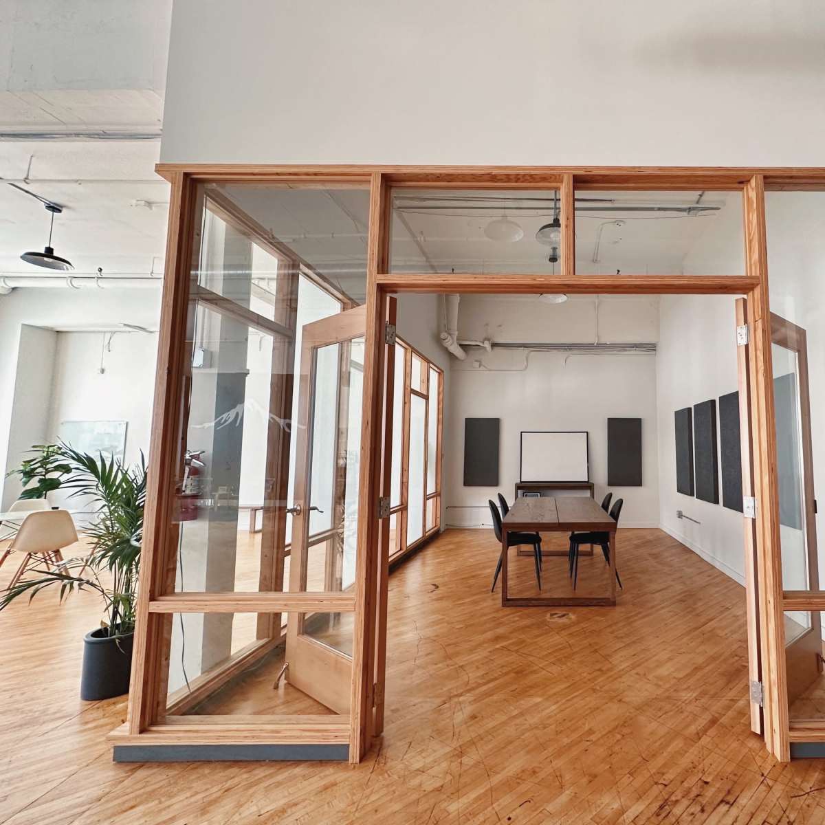 A large, empty conference room with a long wooden table is visible through glass doors framed in wood, surrounded by white walls and wooden flooring.