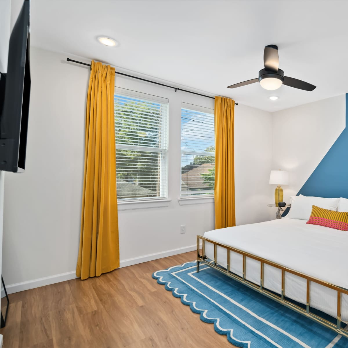 A bedroom with a queen-sized bed, two bedside lamps, yellow curtains, and a blue accent wall.
