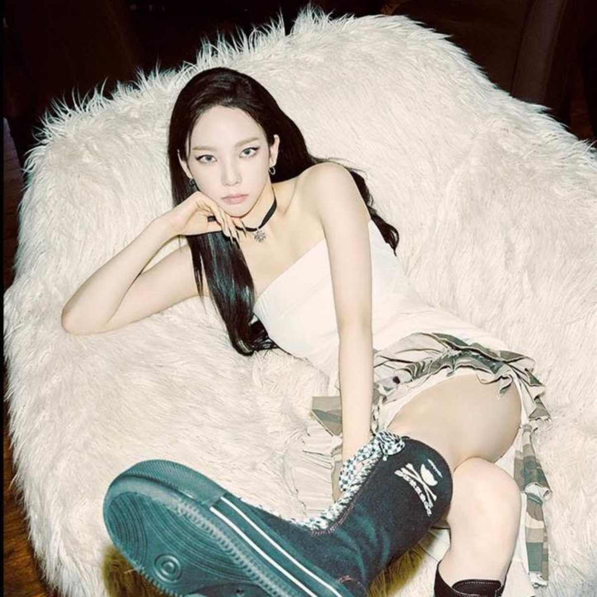 A person lounges on a plush, oversized chair while wearing a short dress and knee-high boots.